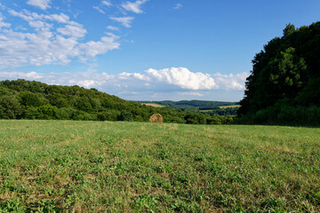 A beautiful summer day in the countryside, showcasing a green field, hay bale, and blue sky.