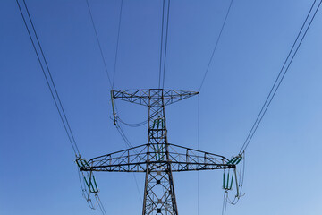 A majestic electricity pylon stands tall, its cables reaching across a clear, blue sky.