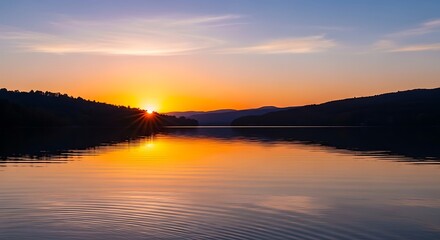 Fototapeta premium Golden sunset reflection on a calm lake with silhouetted hills.