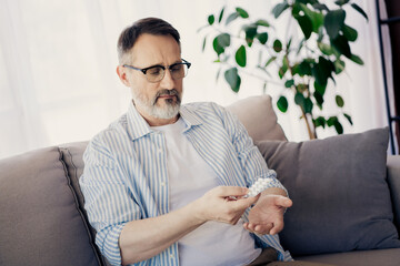 Mature professional man sitting indoors while examining a medicine strip attentively
