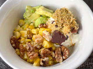 Creamy yogurt bowl with sweet corn, avocado, walnut, chocolate chunk and shredded pastry, bright homemade snack with contrasting textures and cozy