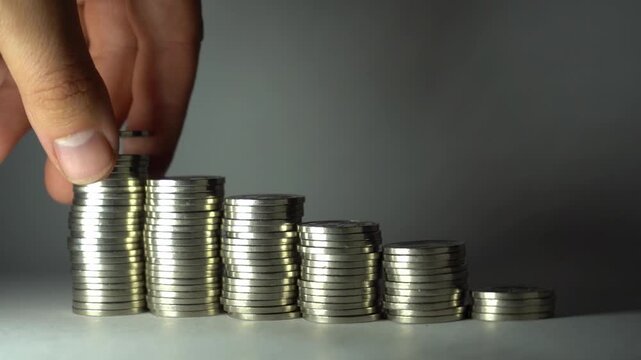 Hand removes coins from a tall stack and places them below, showing fund redistribution, spending control, cash-flow adjustment, and practical money management.
