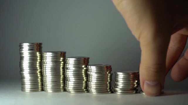 Hand removes coins from a tall stack and places them below, showing fund redistribution, spending control, cash-flow adjustment, and practical money management.