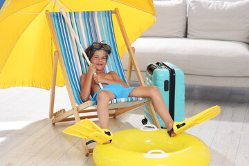 Dreaming about vacation at sea. Little boy with diving mask and flippers on deckchair near inflatable ring indoors