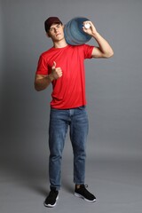 Naklejka premium Delivery man with cooler bottle of water showing thumbs up on grey background