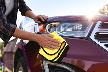 Man wiping car with yellow microfiber rag outdoors, closeup