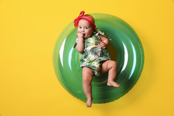 Cute little baby in headband with inflatable ring on yellow background