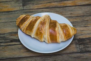 French croissant on wooden tabletop. Fresh croissant on wooden table. Golden baked croissant on wooden background.