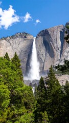 Majestic waterfall cascading down a granite cliff face, framed by lush green trees