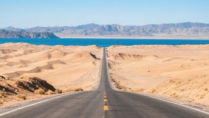 A straight road stretches through a desert landscape toward a distant blue lake with mountains in the background.