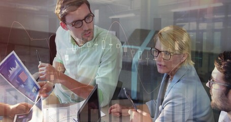 Finance team analyzing market data around conference table at office, with charts and laptops