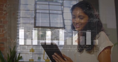 Indian woman wearing blouse, holding tablet analyzing data overlay in loft office, with window
