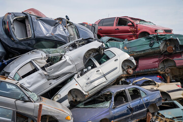 Stacked wrecked cars in a chaotic junkyard under a clear sky, symbolizing automotive waste and recycling.