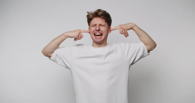 Man expresses frustration by covering ears while making funny faces against a plain background