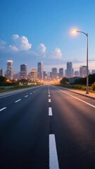 Fototapeta premium Wide urban highway leading toward a city skyline at dusk with illuminated streetlights and modern high-rise buildings in the background.