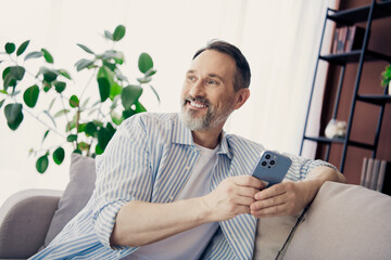 Handsome professional man using smartphone seated indoors in a casual home setting, enjoying leisure time on a sunny day