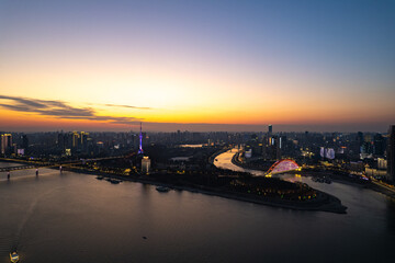 Wuhan Yangtze River Hubei cityscape glows under the twilight sky, a vast river embracing the illuminated urban landscape.