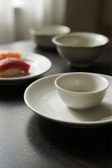 White ceramic bowl and plate set on dark table with sushi in background