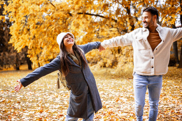 Happy young couple holding hands in colorful autumn park, enjoying love and togetherness in fall season.