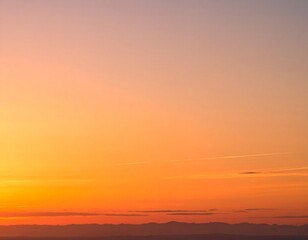Fototapeta premium Vibrant orange and yellow gradient sky at sunset with a distant dark horizon line.