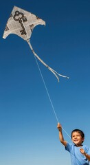 Child joyfully flies a unique kite made of newspaper against a clear blue sky in the afternoon sunlight