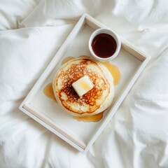Stack of Golden Pancakes with Butter and Syrup on a White Tray in Bed