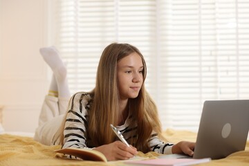 Teenage girl studying online with laptop on bed at home
