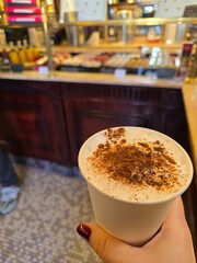 Hand holding cappuccino with cocoa in cozy cafe