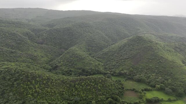 Aerial drone video of lush green Aravalli mountains near Rajsamand and Udaipur in Rajasthan, India, filmed after the monsoon season with dramatic cloudy skies enhancing the scenic landscape view.