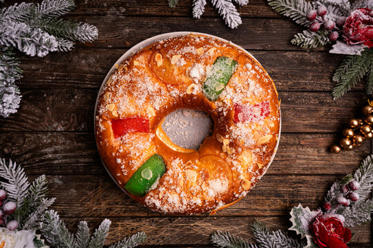 Roscon de reyes with cream and christmas ornaments on a wooden background, top view. Roscon is a traditional Spanish Christmas pastry cake with decoration. Kings day concept spanish three kings cake.