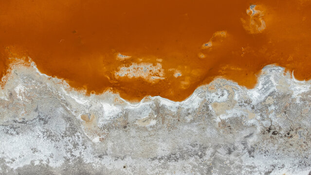 An abstract aerial view of the vibrant, colorful shoreline of a high-altitude salt lake, where deep red mineral waters meet white salt deposits