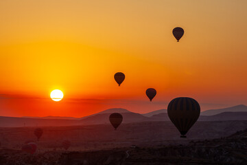 Hot air balloon flying over rocky landscape at sunrise in Cappadocia. Turkey