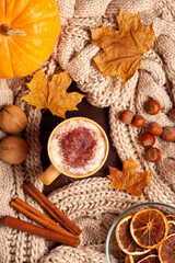 A top-down view of a cozy autumn arrangement featuring a mug of pumpkin spice latte, a warm knitted blanket, pumpkins, and fall leaves.