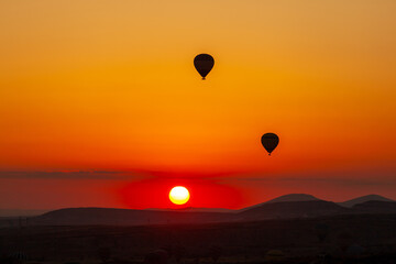 Hot air balloon flying over rocky landscape at sunrise in Cappadocia. Turkey