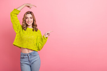 Cheerful young woman in a trendy yellow sweater posing against a vibrant pink background with a...