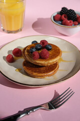 Pancakes with berries on a pink background. A bright summer breakfast with harsh lighting. 