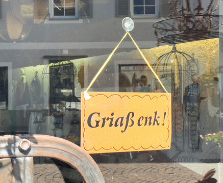 Lienz, Austria - September 18, 2025: Sign reading "Gri enk!" hanging in a shop window, showcasing local culture and inviting customers to enter the store with a warm greeting