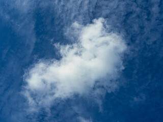 Single puffy cumulus cloud floating against deep blue sky with delicate cirrus texture, minimal weather background with generous copy space