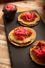 Panuchos, a typical dish from Yucatan, Mexico. A handmade, fried corn tortilla filled with beans, topped with cochinita pibil, pickled red onion, and habanero pepper.