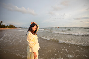 Beautiful Asian woman is happily strolling along the beach as the waves crash against her back. Happy girl rejoices in summer vacation.