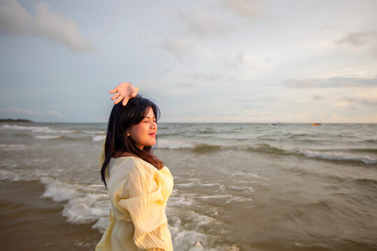 Beautiful Asian woman is happily strolling along the beach as the waves crash against her back. Happy girl rejoices in summer vacation.