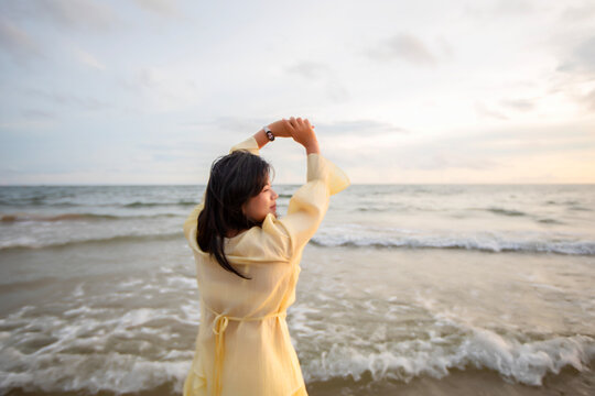 Beautiful Asian woman is happily strolling along the beach as the waves crash against her back. Happy girl rejoices in summer vacation.