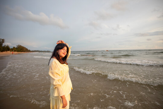 Beautiful Asian woman is happily strolling along the beach as the waves crash against her back. Happy girl rejoices in summer vacation.