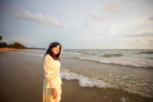 Beautiful Asian woman is happily strolling along the beach as the waves crash against her back. Happy girl rejoices in summer vacation.
