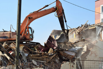 Fototapeta premium A modern excavator removes the rubble of a demolished residential building.