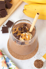 Chocolate banana peanut butter smoothie in a glass on white kitchen table. Healthy blended breakfast drink.