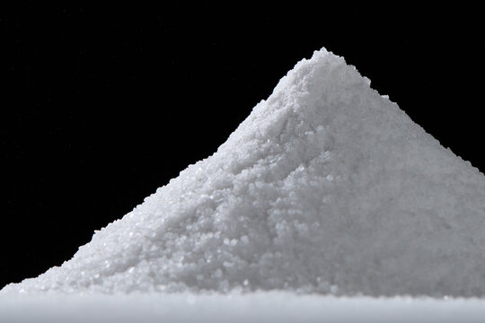 Powdery white substance forming conical pile against dark backdrop, suggesting chemical, culinary, or potentially illicit context