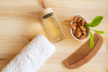 Almond oil bottle, almonds in a bowl, wooden comb and white towel on a light wood background,...