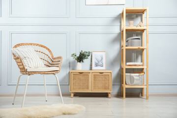 Stylish armchair with pillow, cabinet and decor indoors. Interior design