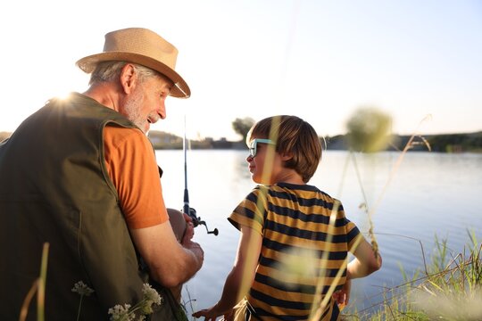 Happy grandfather and his nephew fishing together near river outdoors